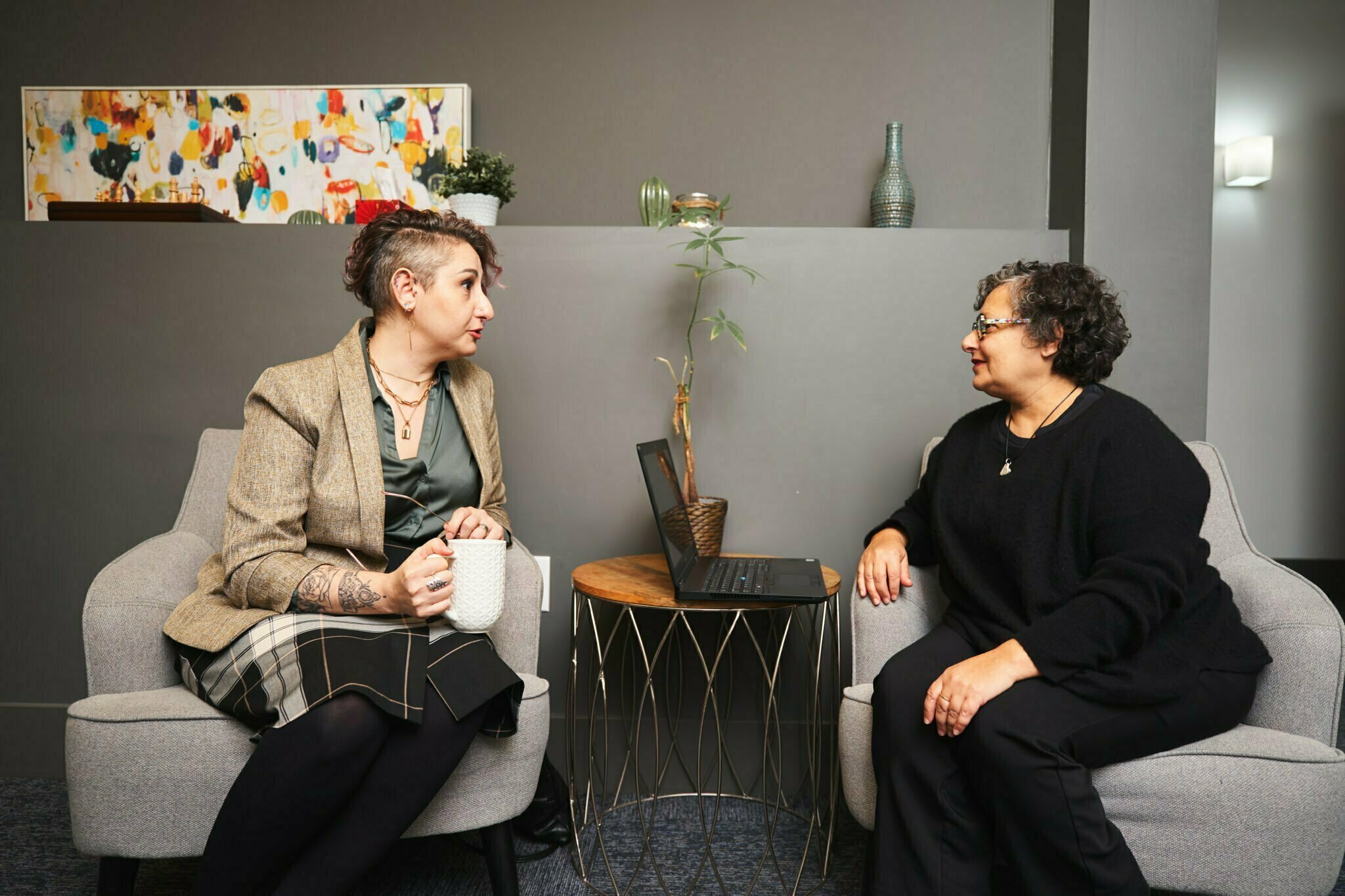 two coworkers sitting in the office discussing work over a cup of coffee